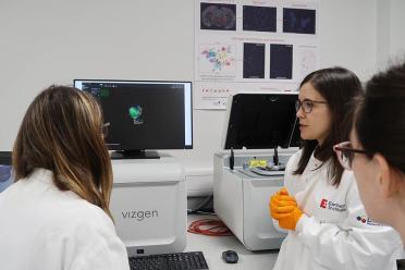 Scientist in white lab coat and orange safety gloves explaining the Vizgen Merscope spatial equipment